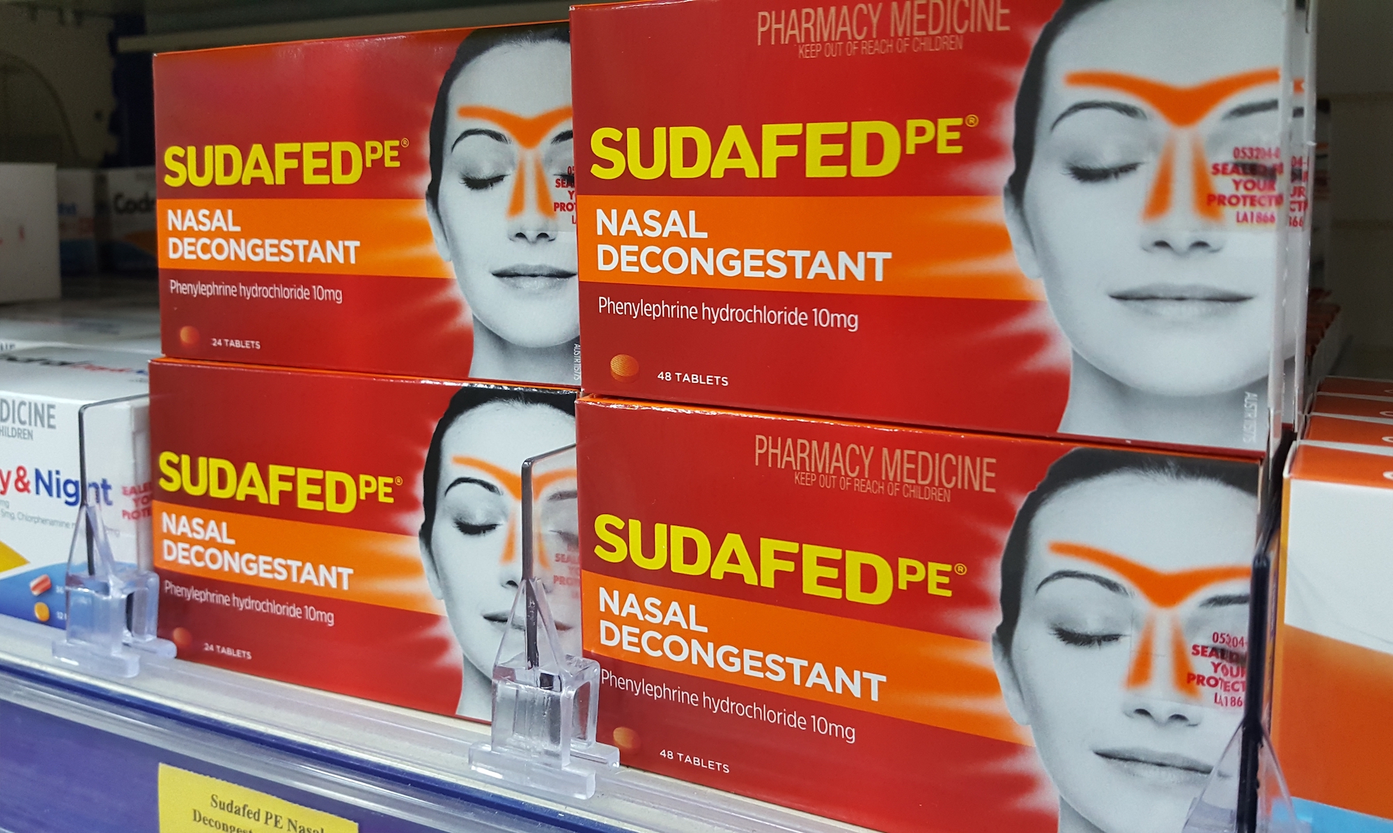 Four red boxes of Sudafed PE stacked on a shelf