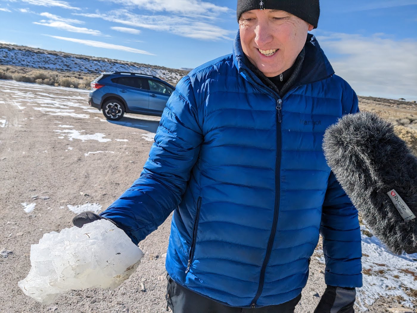 A man holding a white crystal the size of a loaf of bread. Outdoors at the Great Salt Lake