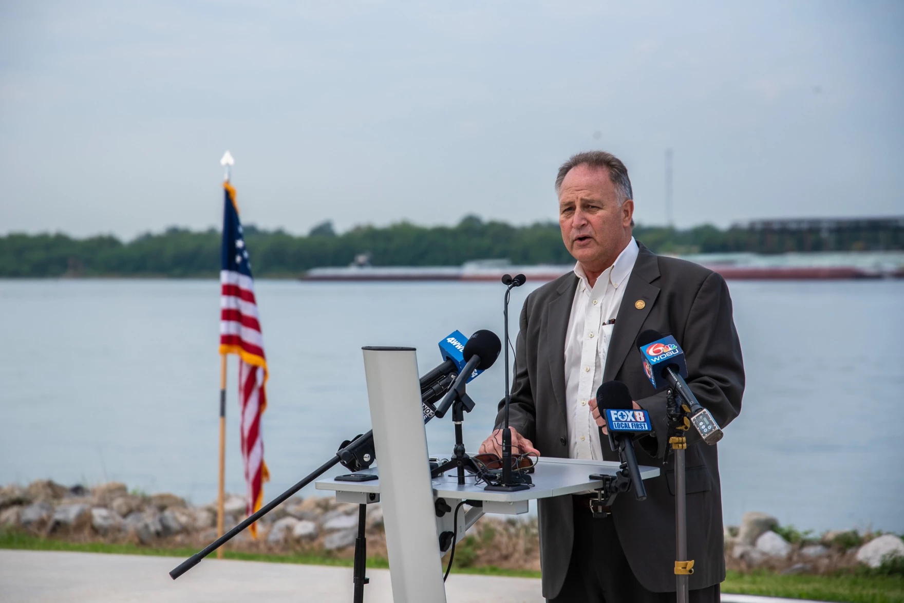 A man in a suit talks at an outdoor press conference. Medium shot