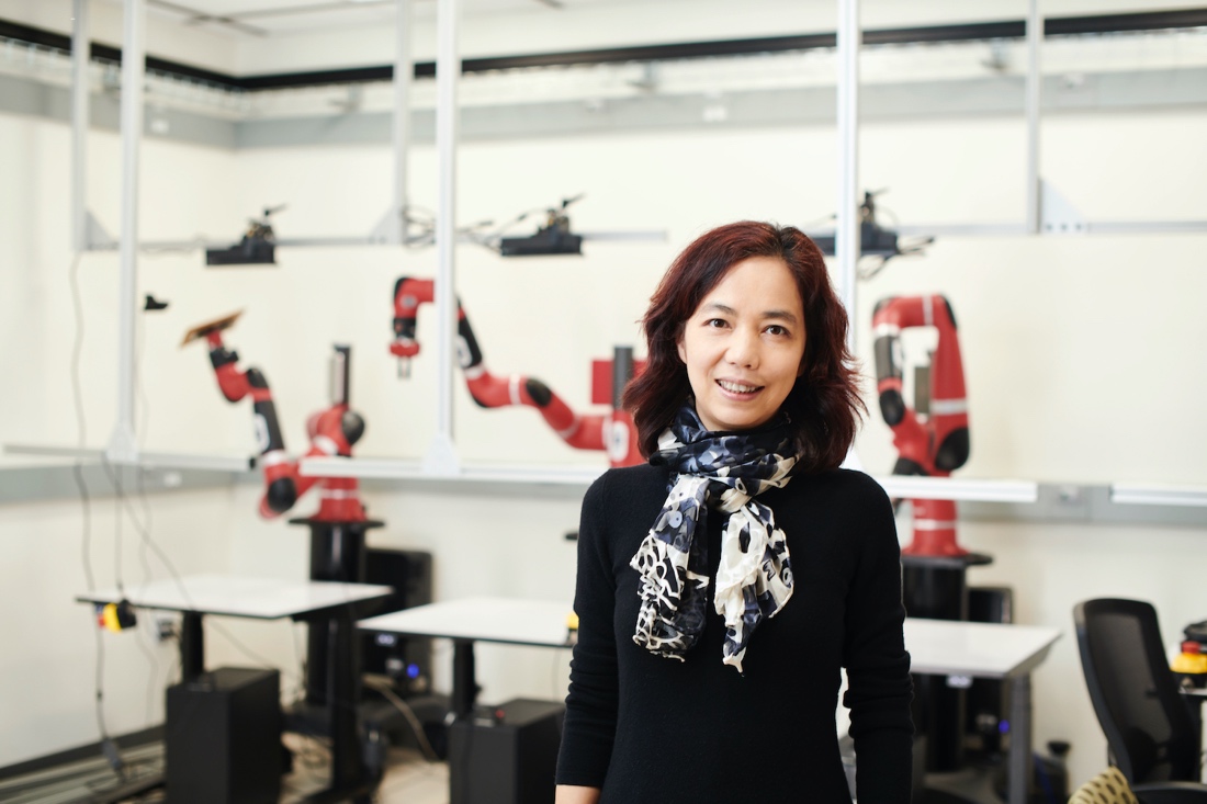 A woman stands in front of a line of robot arms.