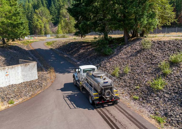 A truck with a tank on the back drives up a hill.