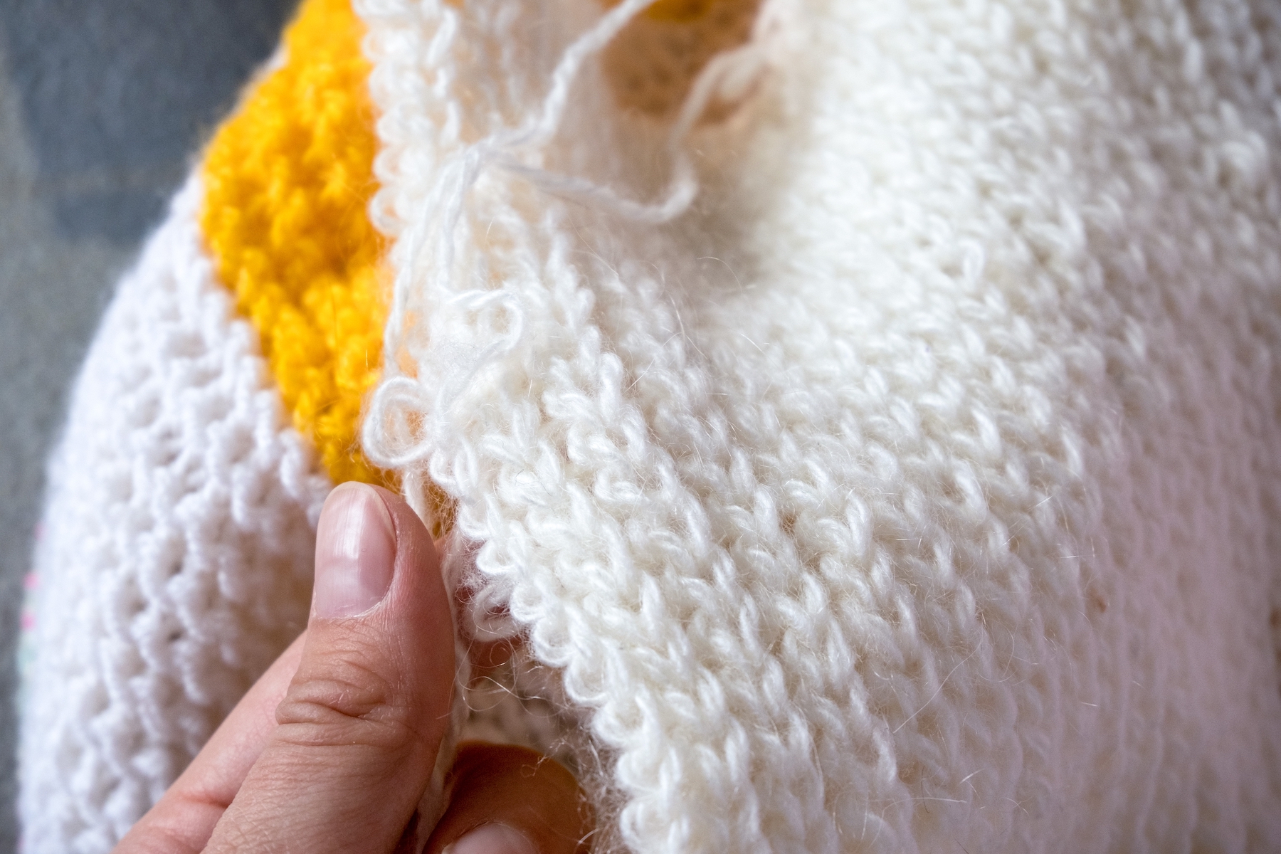 Unraveling a knitted product. The hand pulls the threads from the knitted fabric.