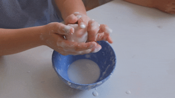 A child handling a white object, rolling it into a stiff ball. When the child stops, the ball melts into a liquid-like flow.