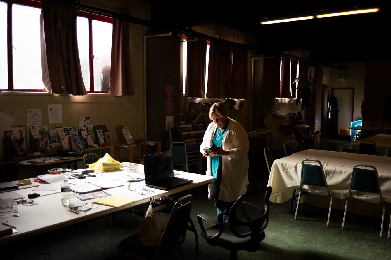 A woman standing in a darkened room reads a small book.