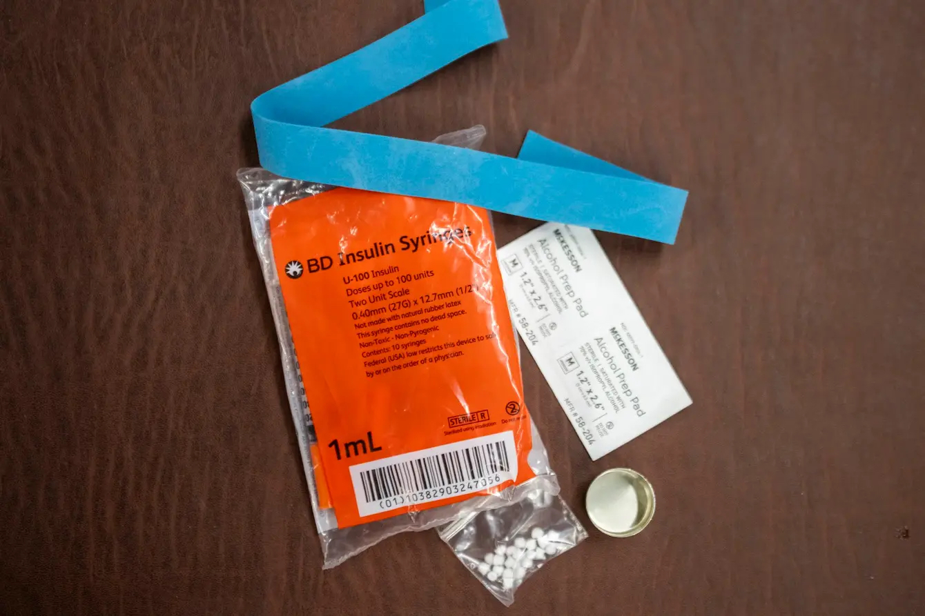 A plastic bag that reads "insulin syringes" with a tourniquet and a bottle cap.