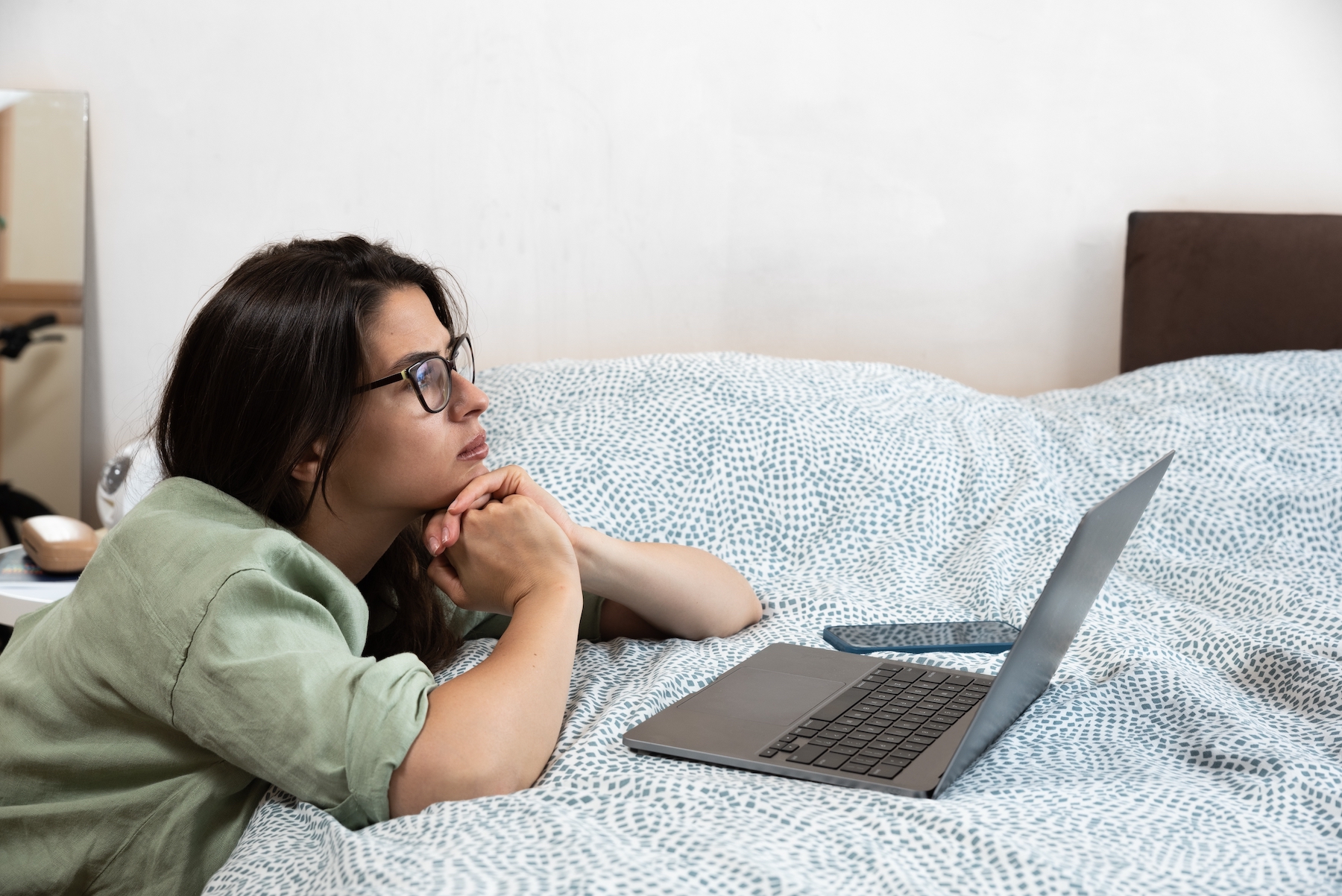 A young woman looking at her laptop on her bed.