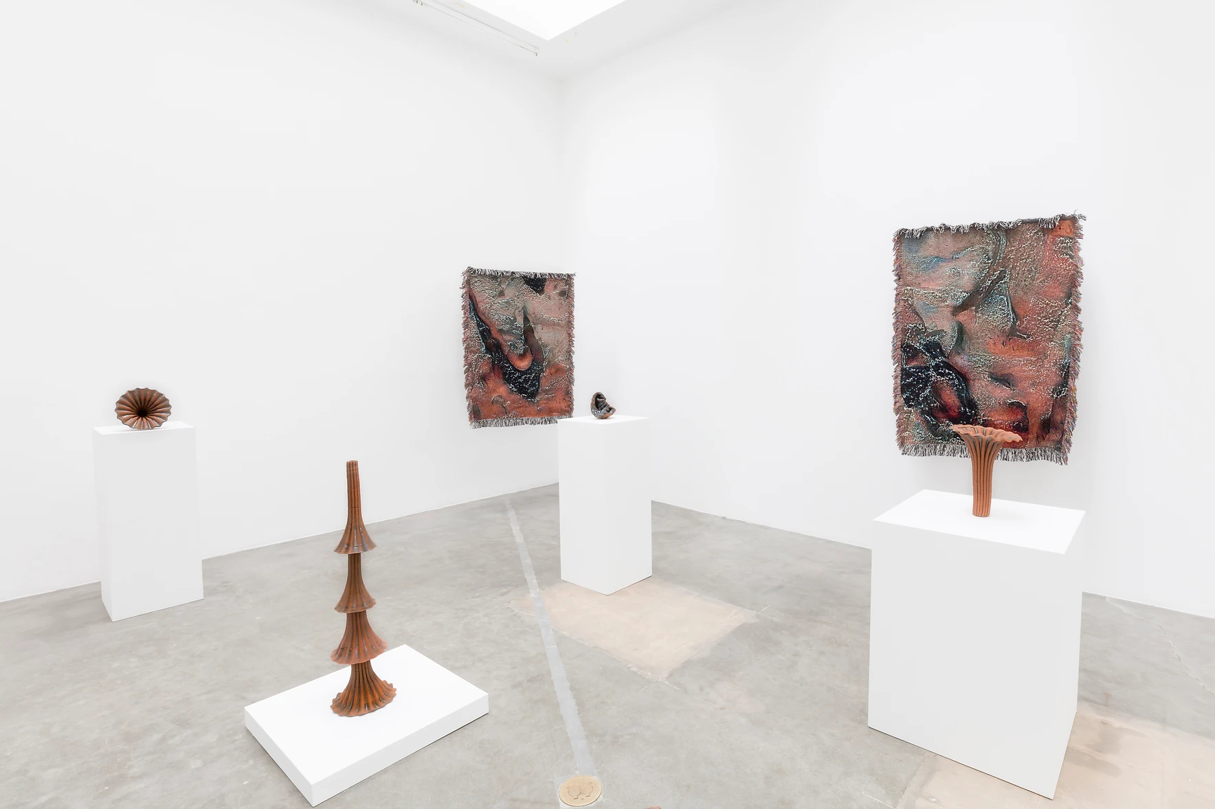 A gallery with white walls of ceramic sculptures and hanging textiles
