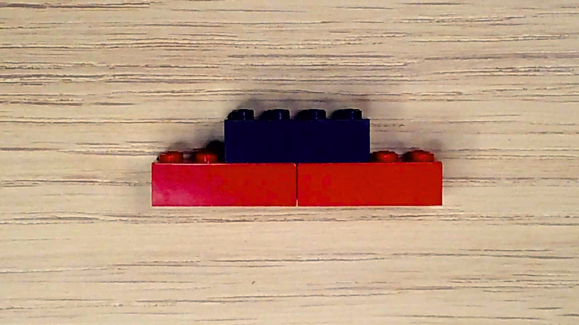 Two red 2x4 plastic bricks with on black 2x4 brick attached to the top, bridging the red bricks.