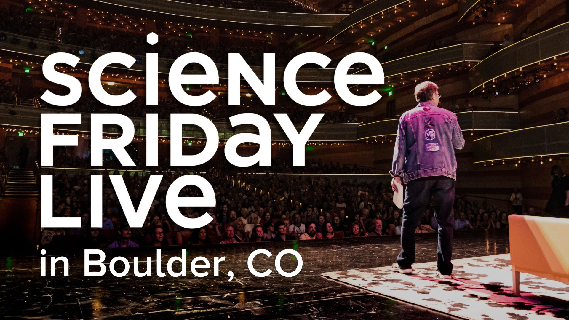 Ira Flatow stands on a stage addressing a live audience in a large auditorium. He faces away from the camera. Text reads "Science Friday Live in Boulder, CO"