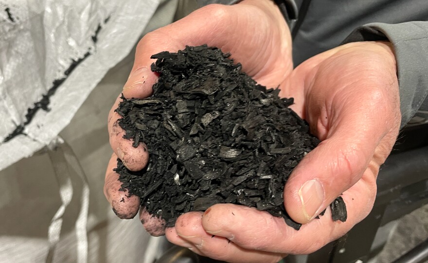 A pair of hands holding a pile of black dirt-looking stuff.