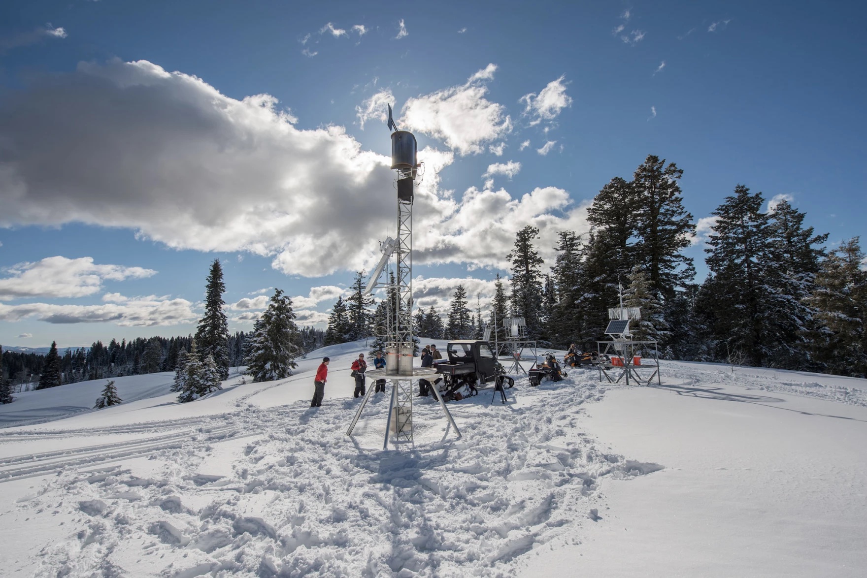 An antenna/metal structure that's about 20 feet high stands at the top of a snowy area.