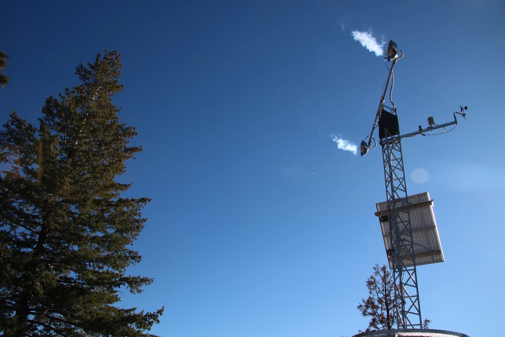 A metal tower with a structure emitting steam on the top.