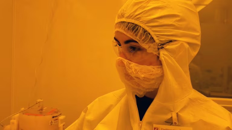 A person in a full body PPE suit stands in a room with yellow lighting