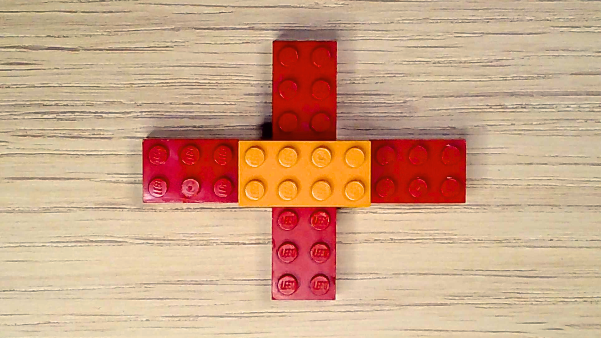 Four red 2x4 bricks are arranged in a cross form, with an orange 2x4 brick placed on top of the cross to connect all the red bricks.
