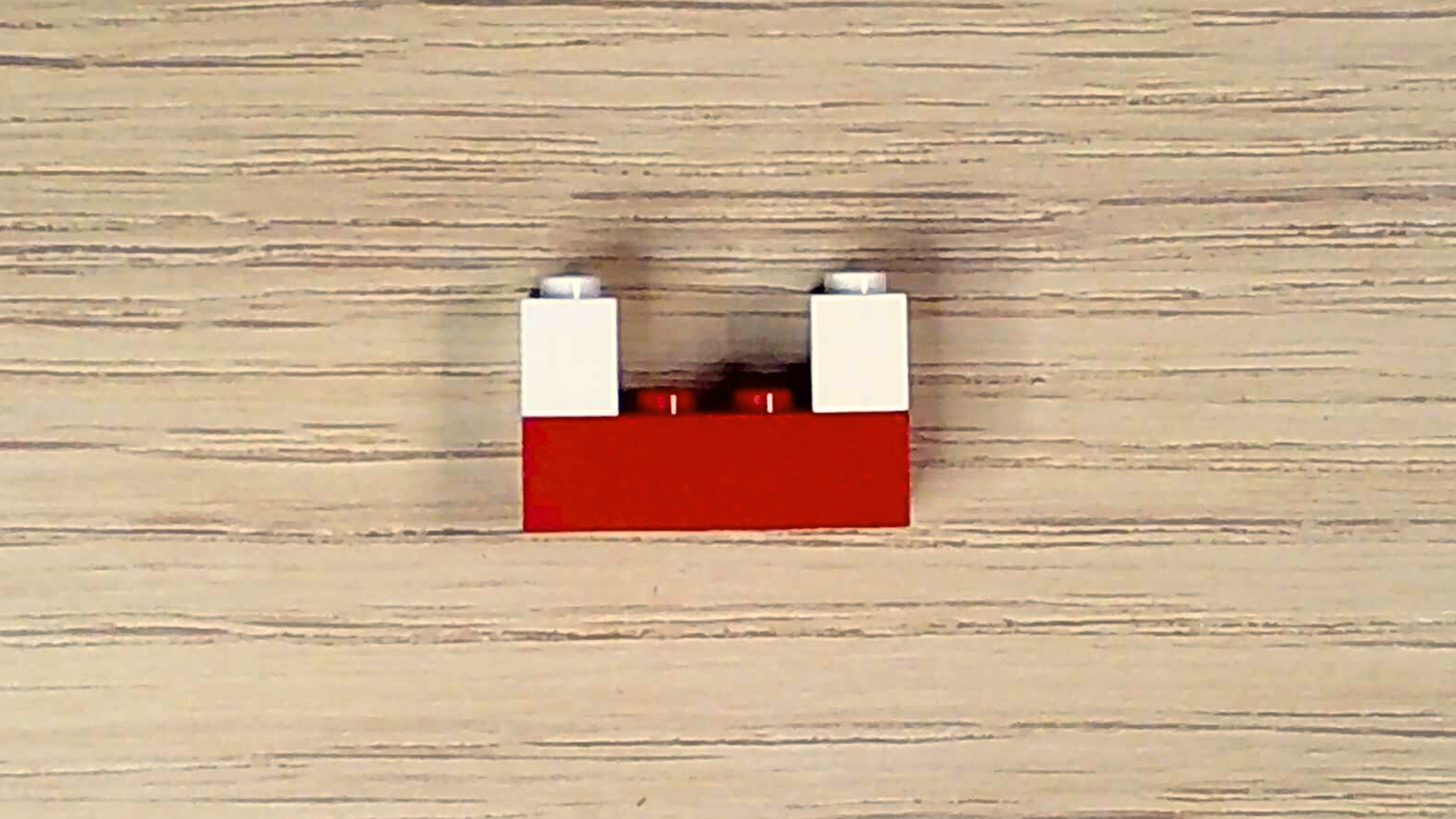 A red 2x4 plastic brick with two white 1x2 bricks attached in a U formation.