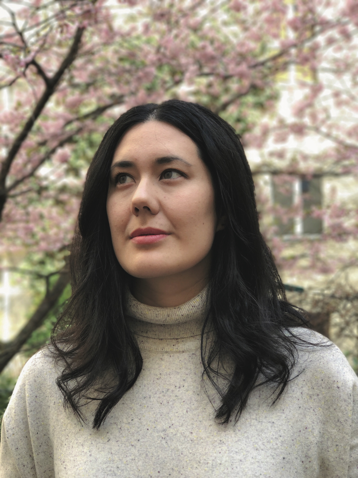 A woman looking to the left with flowering trees in the background.