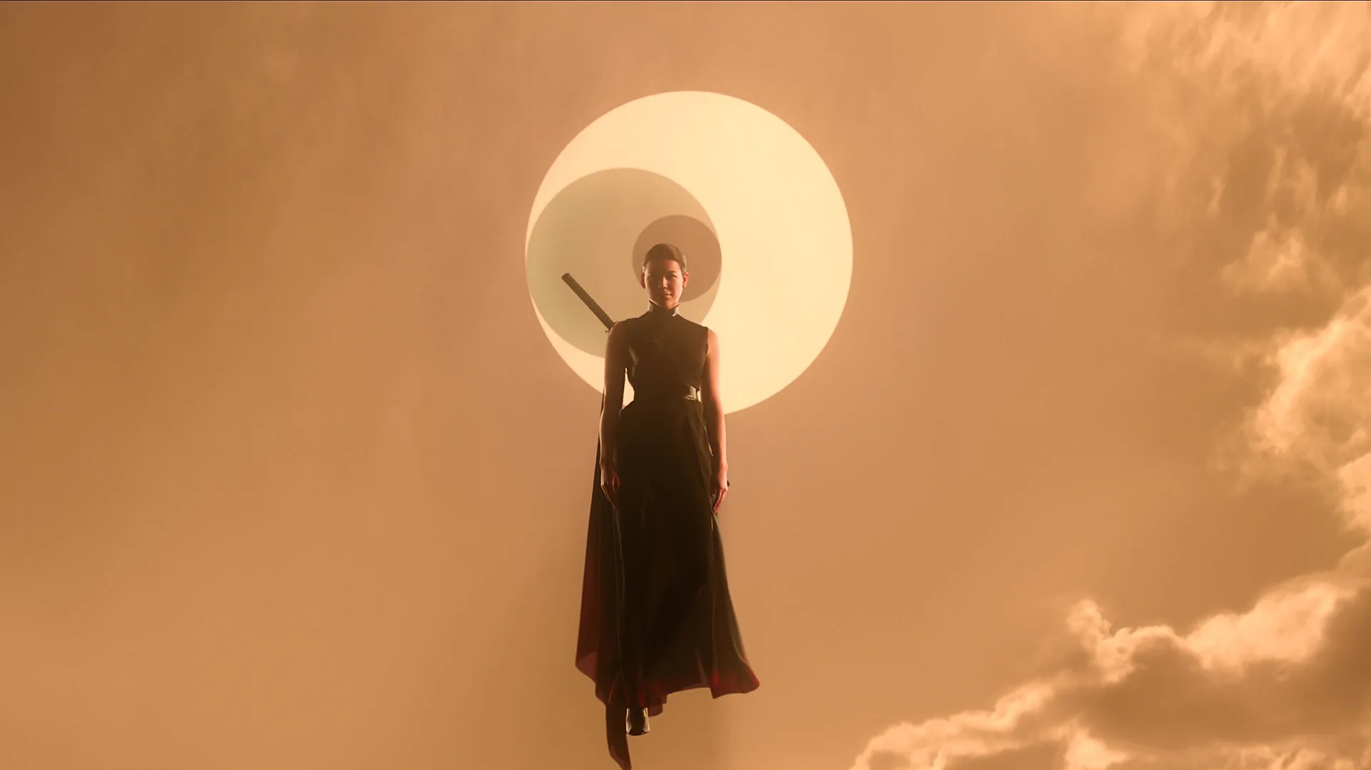 a woman wearing a forboding black dress with a sword against her back hovers against an orange sky in front of a simple graphic of three circles, each smaller than the next, enclosed in one another