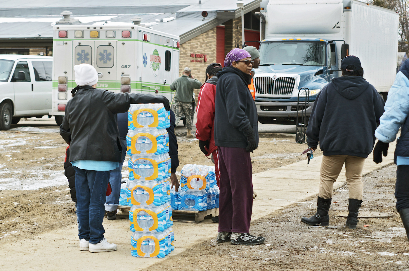 A few people standing around cases of bottled water outside a fire station.