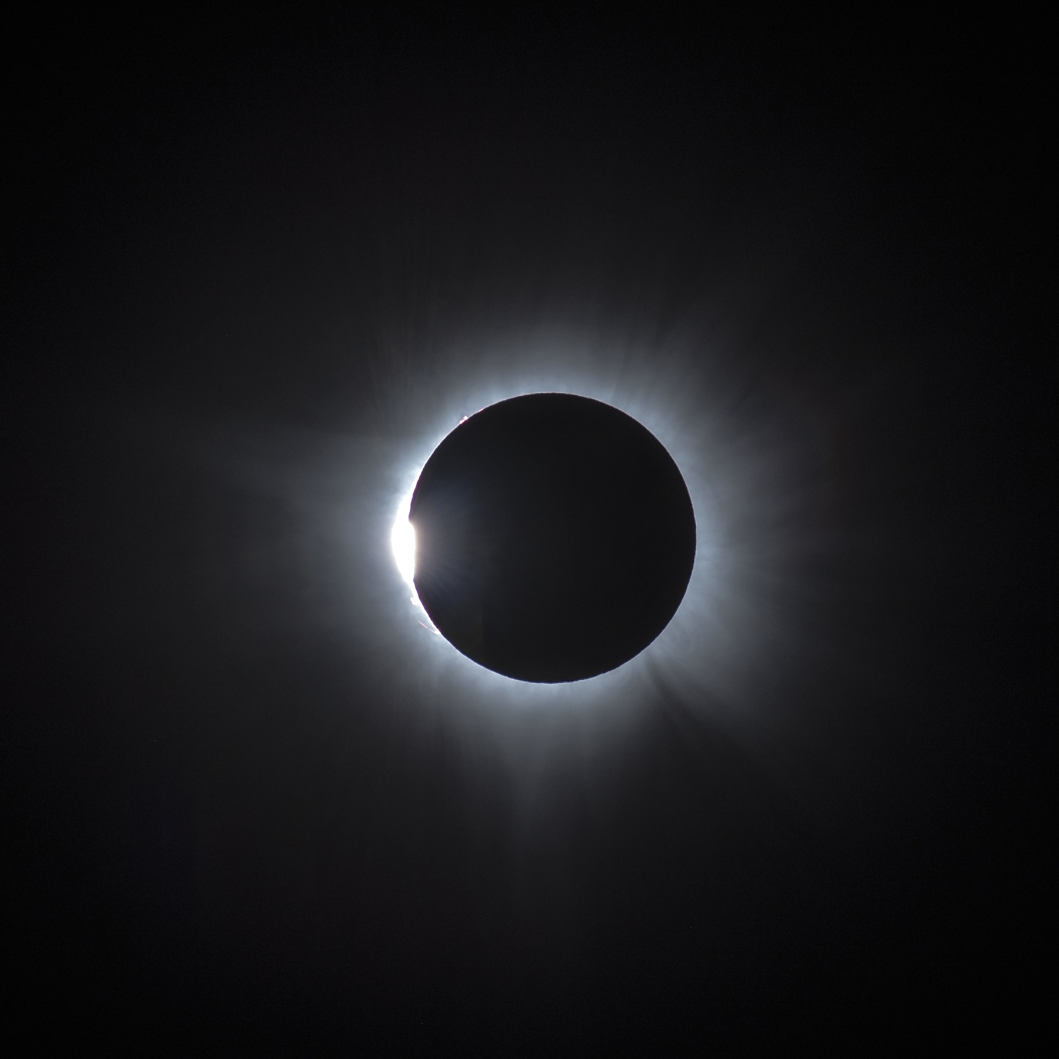 A straight-on view of eclipse totality. A silver ring in a dark sky, with a flare of round light on the lower left part of the ring.