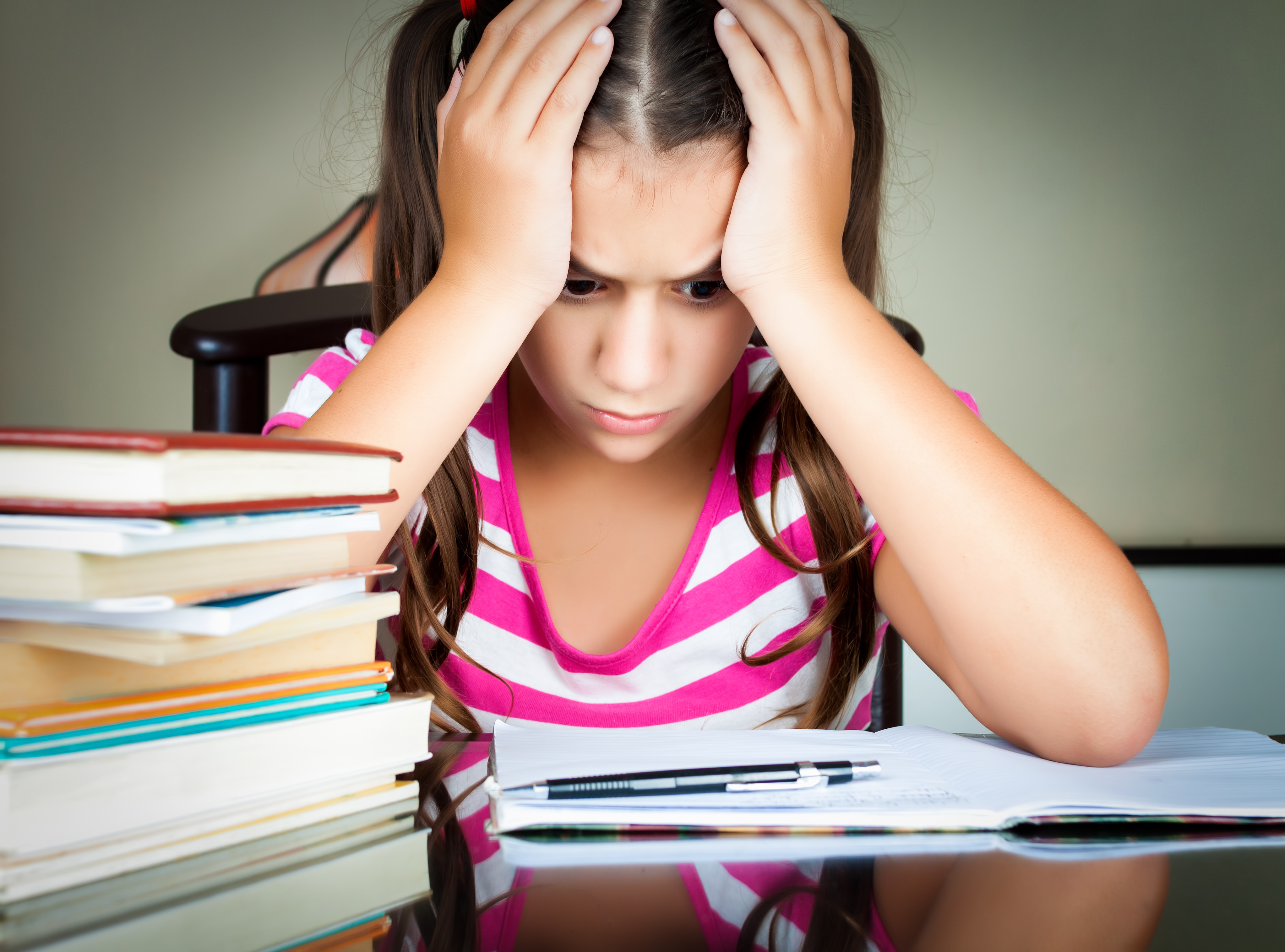 Una estudiante frustrada con su cabeza entre sus manos mira a un libro de texto guía abierto.