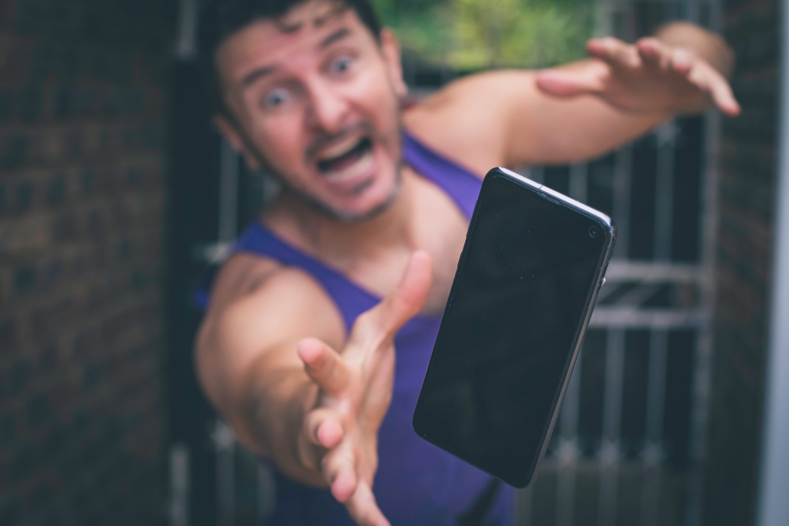 An upset-looking man reaches for a dropping smartphone.