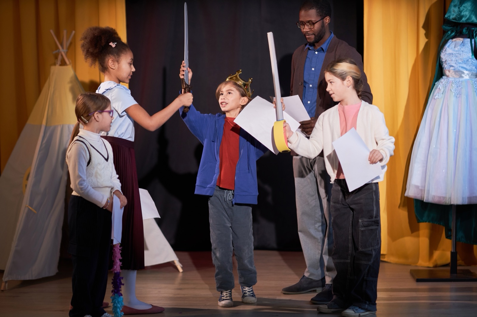 Niños ensayando una obra escolar en el escenario en un teatro con un príncipe recitando líneas.