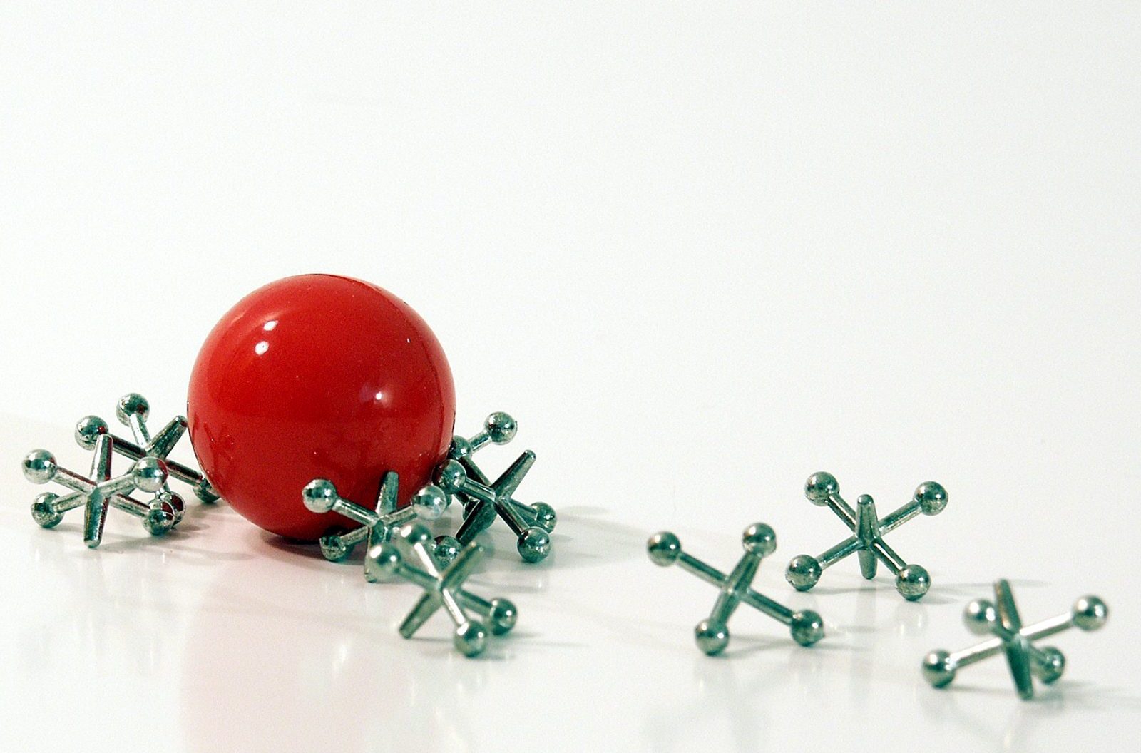 A small, shiny red ball with several metal jacks on a white background.