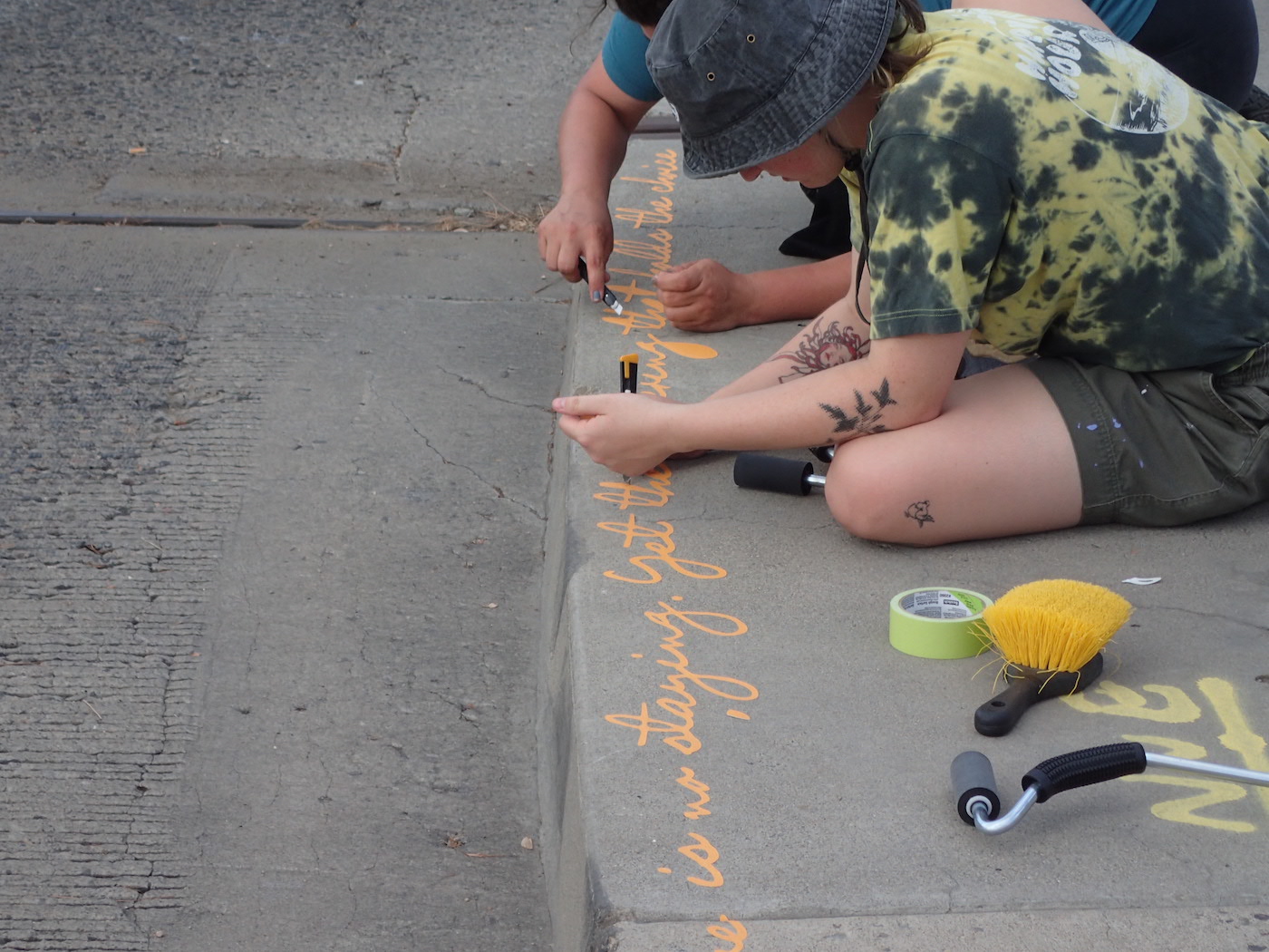 Two people writing orange poetry along the curb of a sidewalk.