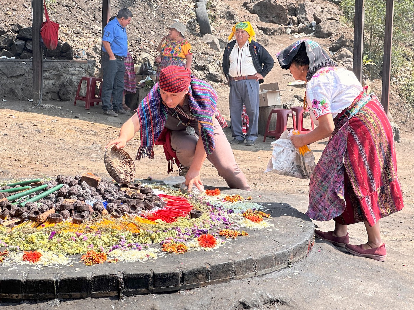 Two people wearing colorful clothing are putting various objects onto a raised circular platform.