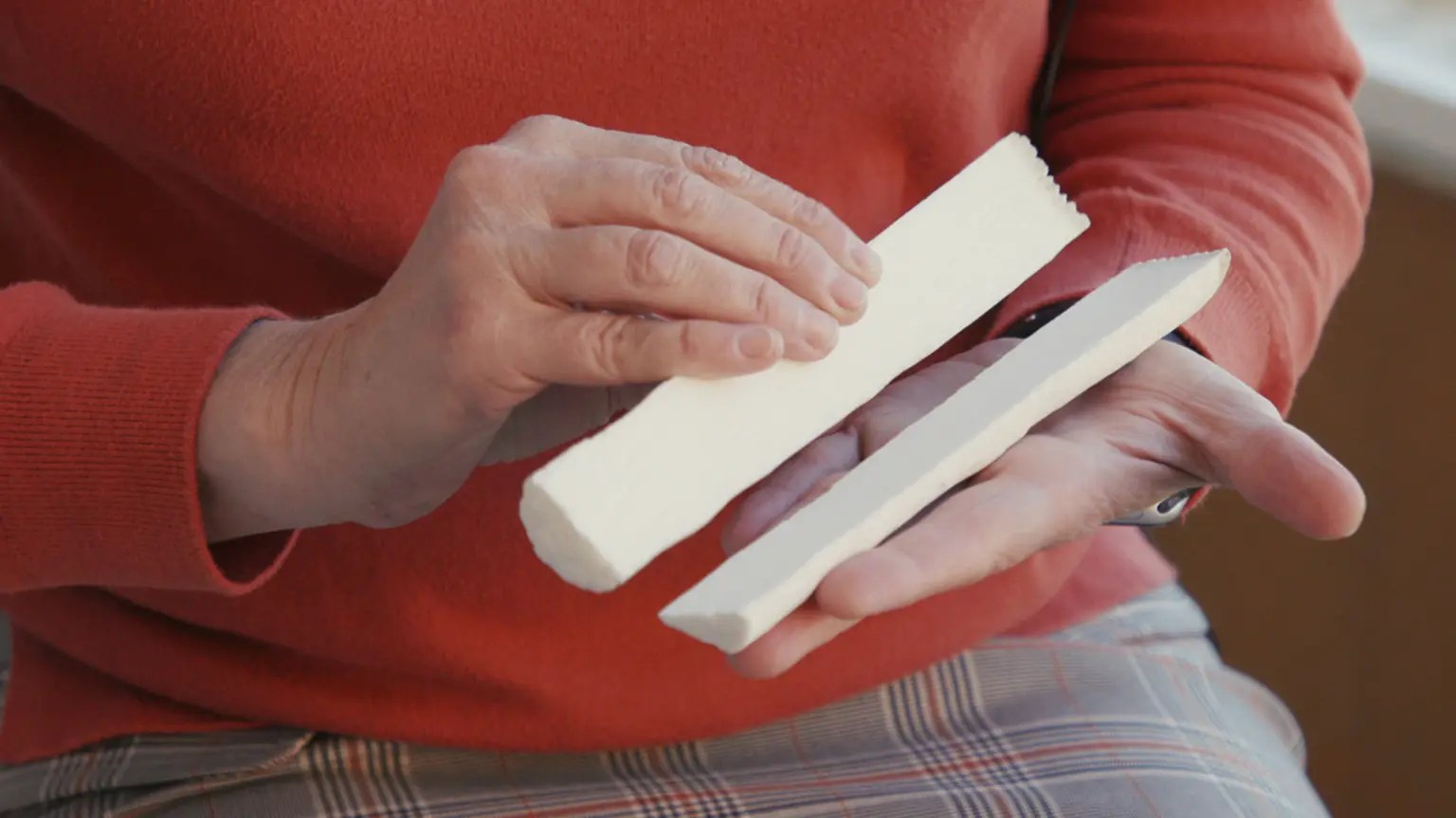 A person's hands hold a white cylinder divided in half hot dog style