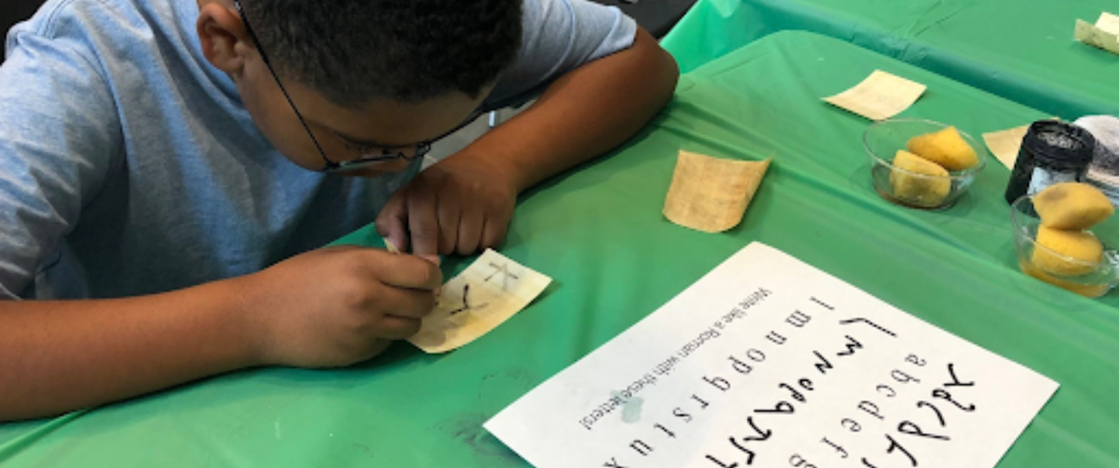 A young child writes on papyrus paper with dark ink.