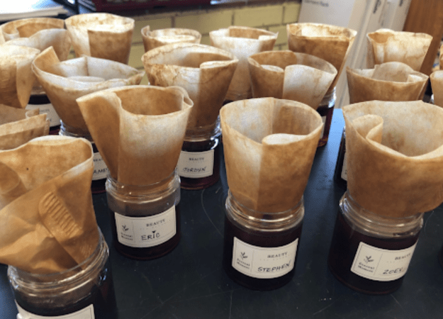 Several labeled glass jars hold dark brown liquid with brown coffee filters positioned on top.