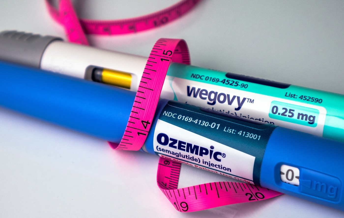 Ozempic and Wegovy pens wrapped in a pink tape measure on white background