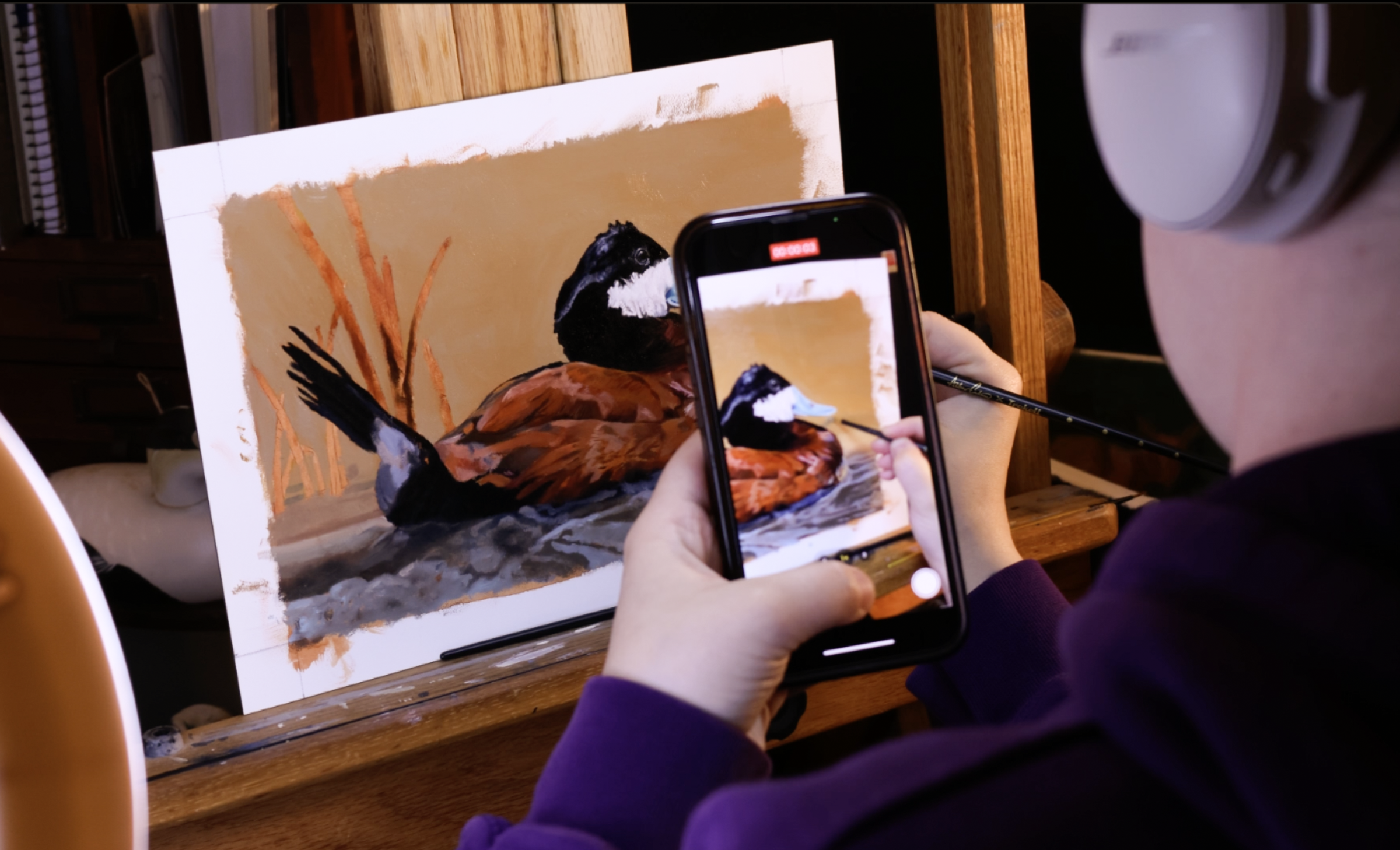 A person holding a phone taking a video up to a painting of a ruddy duck, which they're entering in the 2025 Federal Duck Stamp Art Contest.