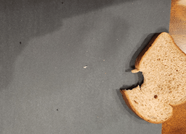 Piece of whole-wheat bread with a bite taken out sitting on a piece of black construction paper on a wooden table.