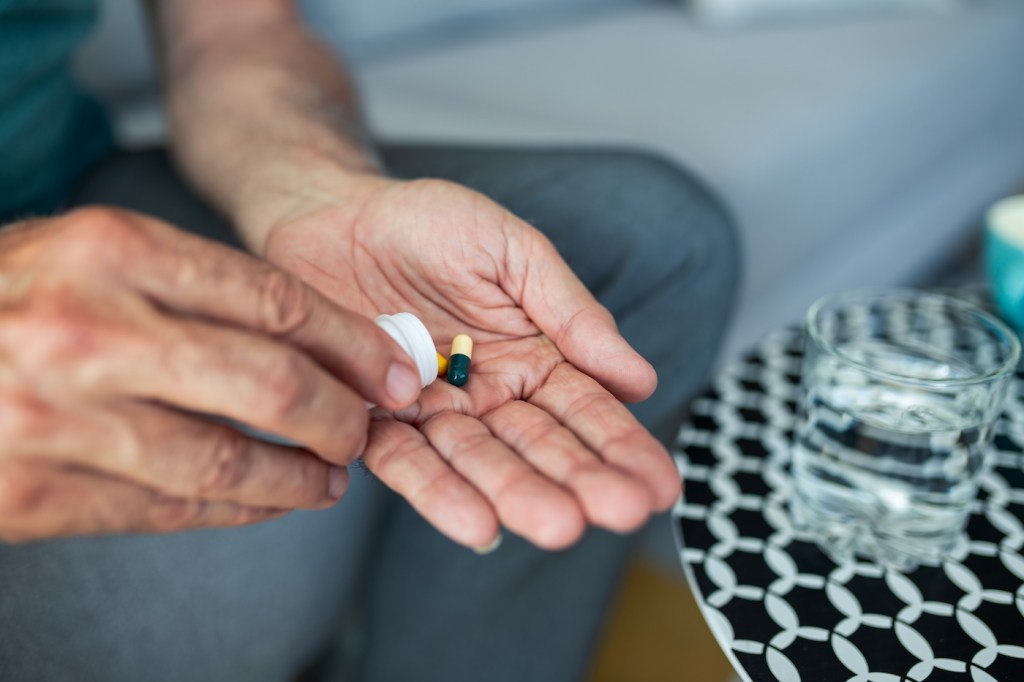 A senior man, feeling stressed and depressed, takes a pill with a glass of water. Depicting the act of self-medication and the impact of antidepressant drugs, use of medicines, SSRI withdrawal