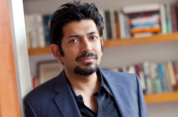 Author Siddhartha Mukherjee standing in front of a bookshelf