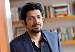 Author Siddhartha Mukherjee standing in front of a bookshelf