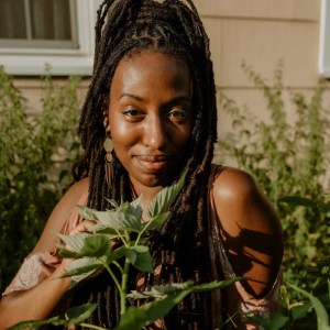 A Black woman surrounded by plants smiles at the camera.
