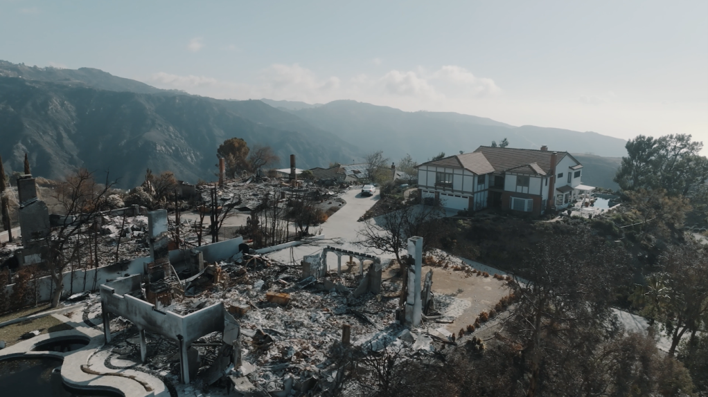 A large home stands unharmed on a mountaintop, while the three houses around it are completely burned down.
