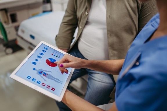 Close up of female doctor consulting with overweight patient, discussing medical report shown on a tablet.