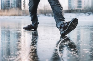 Two legs with black shoes stand on shiny, icy ground, with one sole upturned.