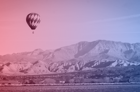 A hot air balloon floats over an arid, brown mountain landscape