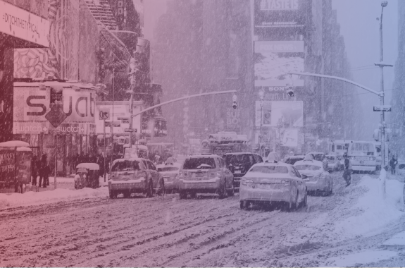 Taxis line up at a stoplight in times square, with slushy snow in the road and more snow falling. Image has a red-to-blue filter over it.