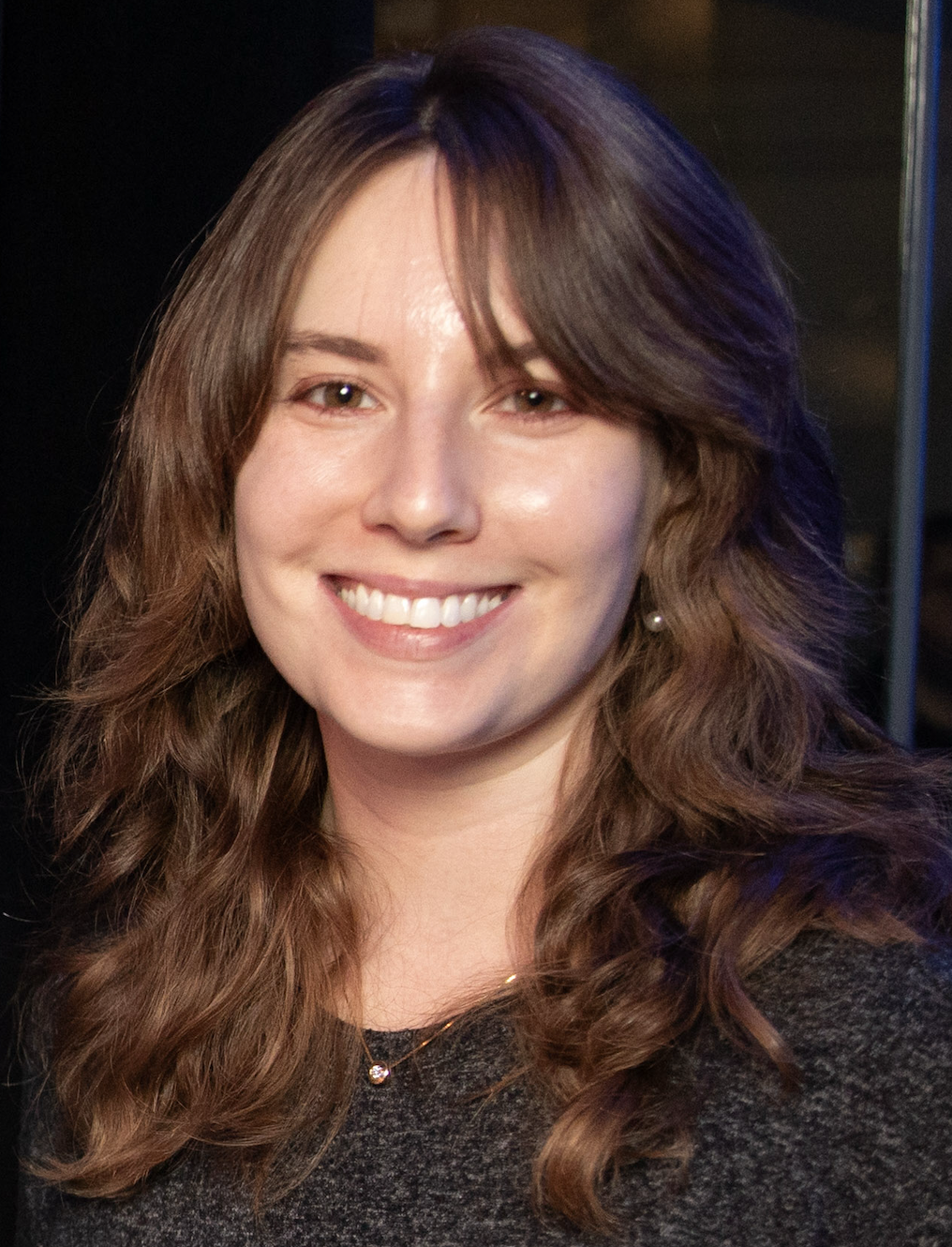 A woman with wavy brown hair smiles at the camera