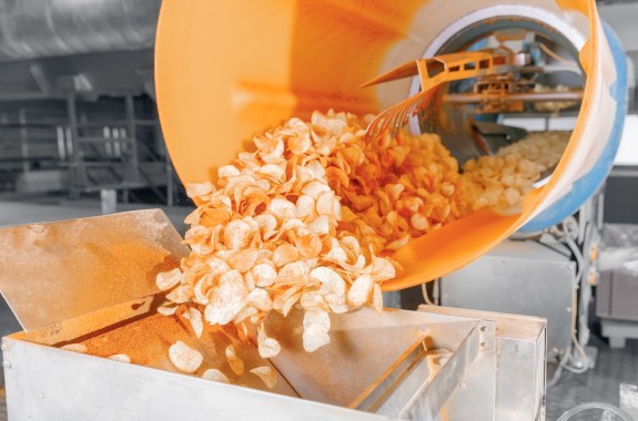 Potato chips fall from an orange cylinder into a metal chute covered in orange powder.
