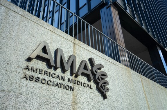 Large black letters spell out "AMA American Medical Association" on a grayish stone wall at the base of a black building.