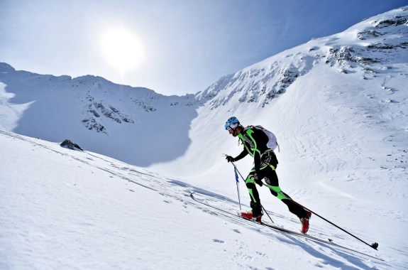 A ski mountaineer skins up a mountain against a sunny sky