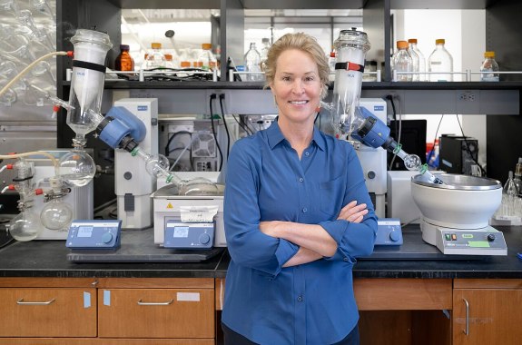 A white woman in a blue shirt stands against a lab bench smiling.