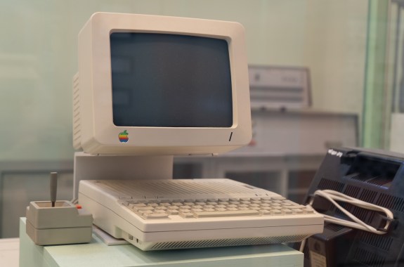 An old desktop computer with small monitor and large white keyboard sits on display against a blurry greenish backround.